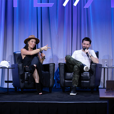 Image of two smiling Full Sail alumni sitting in chairs, speaking into microphones