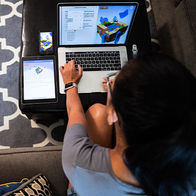 Overhead view of a student working at a laptop with a phone and tablet next to her as she designs a game