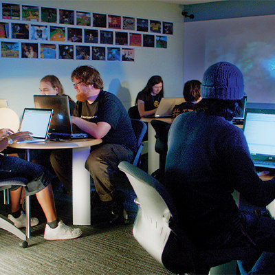 students work in small groups on laptops at small round tables 