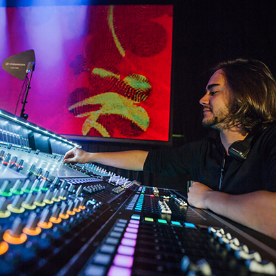 Side angle view of a student mixing on a large board with a large red projection screen in the background