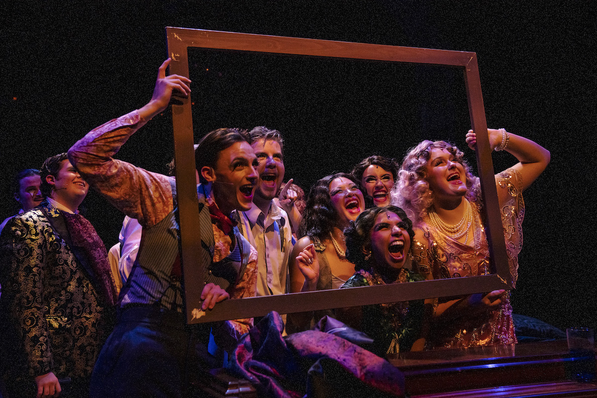 UNCG Wild Party production photo with several actors in 1920s periods dress holding up an empty picture frame and smiling  